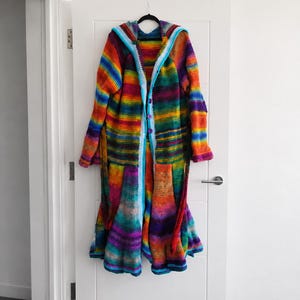 May include: A long-sleeved, hooded crochet cardigan featuring a vibrant, multi-colored horizontal striped pattern in shades of red, orange, yellow, green, blue, and purple. The garment includes a light blue trim along the front opening and hood.