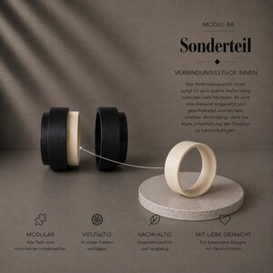 Könnte beinhalten: Ein modulares Verbindungsteil mit der Aufschrift MODUL 8A Sonderteil, bestehend aus zwei schwarzen zylindrischen Elementen mit einem cremefarbenen Innenring. Ein separater cremefarbener Ring liegt auf einem runden Steinsockel, mit Montagehinweis.
