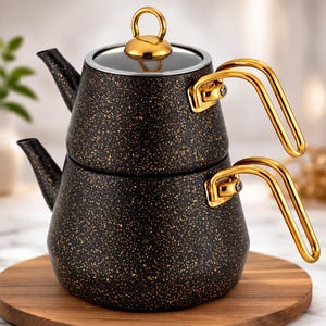Puede incluir: Una tetera negra y dorada moteada con un asa y tapa doradas. La tetera es de metal y se asienta sobre una superficie de madera. La tetera tiene una tapa de cristal y un pico para verter.
