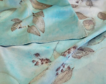 May include: A light blue silk scarf with a pattern of brown leaves. The scarf is folded in half and the leaves are visible on both sides.