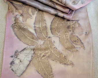 May include: A long, pink silk scarf with a delicate leaf pattern in shades of brown and beige. The scarf is folded in half and the edges are visible.
