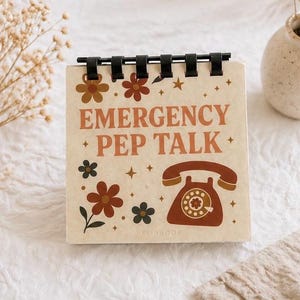 May include: A square flipbook with the words "EMERGENCY PEP TALK" in brown lettering. The cover features a retro telephone illustration and floral designs in brown and black. The flipbook is bound with black rings.