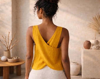 May include: Mustard yellow sleeveless top with a distinctive crisscross back. The top is worn with white trousers. The model is seen from behind. The top is made of a textured material.