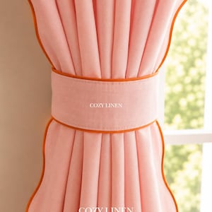 May include: A light pink curtain panel featuring a wide matching tie-back with vibrant orange piping along the edges. The fabric has a visible weave texture and the text COZY LINEN is printed in white on both the tie-back and the lower curtain section.