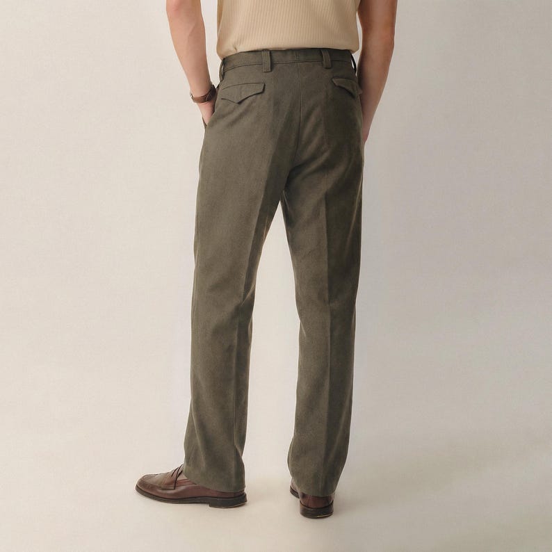 May include: Olive green trousers featuring a structured waistband with belt loops, two rear pockets with buttoned flaps, and a straight-leg cut. The trousers are paired with a light beige shirt and brown leather loafers, shown from the back view.