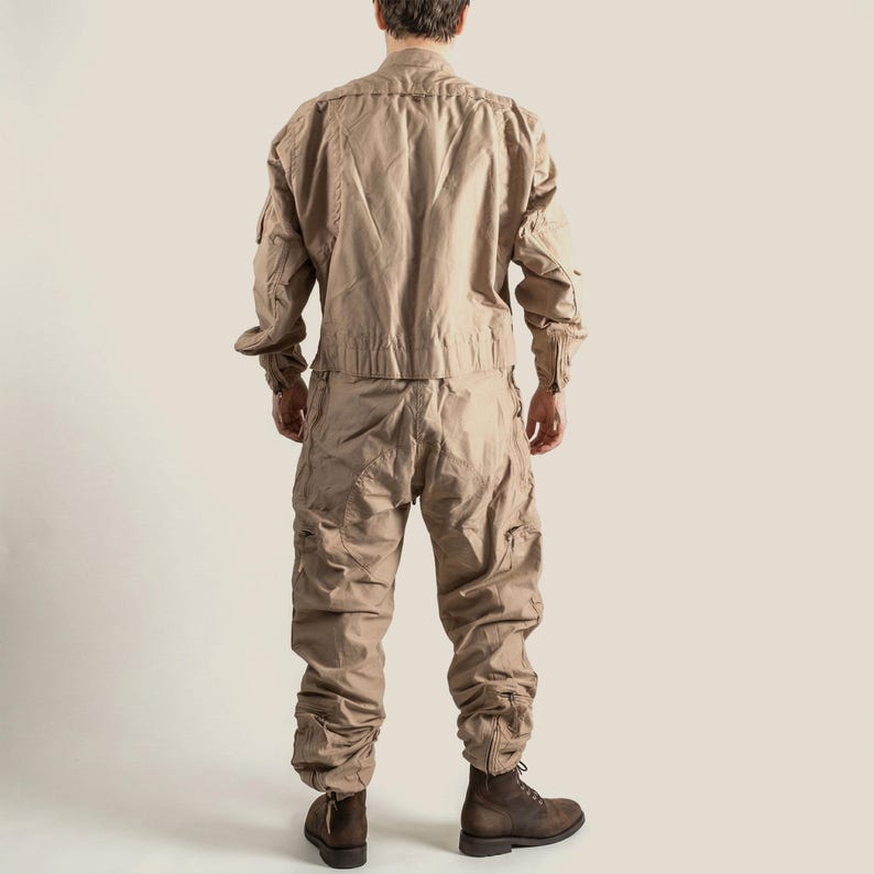 May include: A tan-coloured two-piece jumpsuit with multiple pockets and a collared jacket. The trousers have a gathered ankle design. The person is wearing brown boots. The outfit is made of a lightweight fabric.