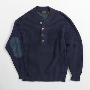 May include: A navy blue long-sleeve sweater featuring a ribbed knit texture, a mock neck collar, and a four-button placket. The garment includes a solid navy blue elbow patch on the right sleeve and a dark interior lining at the neckline.
