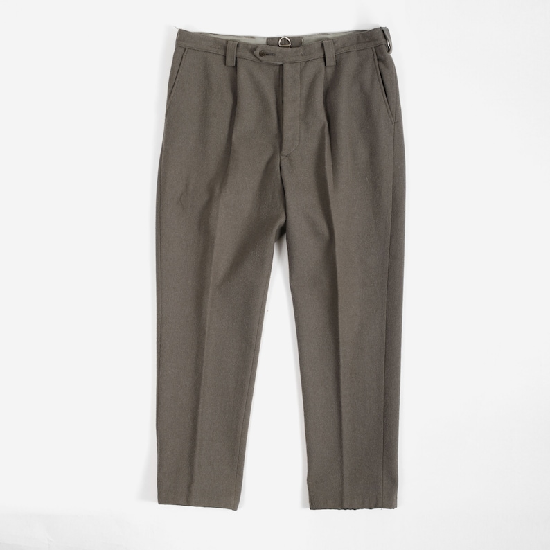 May include: Taupe-colored trousers featuring a high-waisted design with a single button closure, a metal hook-and-eye fastener, belt loops, and two side pockets. The pants have a straight-leg cut with a pressed crease running down each leg.