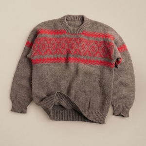 May include: A gray sweater with a red geometric pattern across the chest. The sweater has a crew neck and long sleeves with ribbed cuffs and hem. The knitwear is a warm, cozy style.