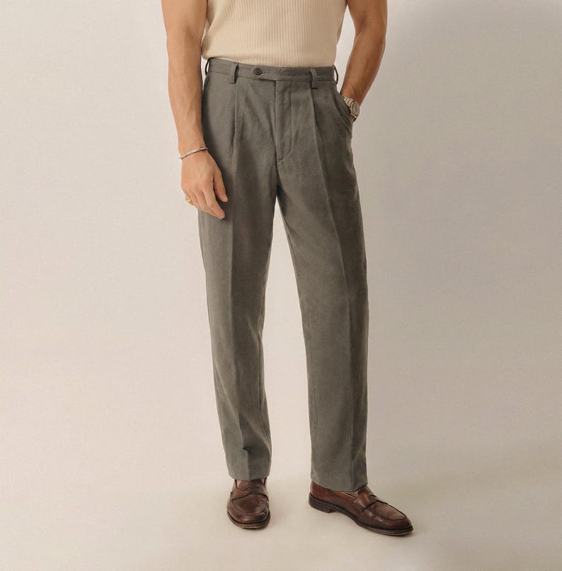 May include: Gray trousers featuring a high-waisted design with a single button closure, belt loops, and a pleated front. These full-length pants have a straight-leg cut and are paired with brown leather loafers, creating a clean and structured look.