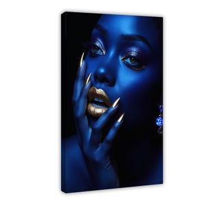 May include: A canvas print featuring a portrait of a person with deep blue skin tones, wearing metallic gold lipstick and matching gold-tipped nails. The person has shimmering eyeshadow and a blue dangling earring, set against a dark background.