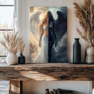 May include: A rectangular wall art print depicting a split figure with a light side featuring a blonde person with white wings and a white dress, and a dark side featuring a dark-skinned person with black wings and a black dress against clouds.