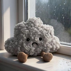 Może przedstawiać: Pluszowa szara chmurka ze smutną miną i małymi brązowymi nóżkami. Chmurka ma kręconą fakturę i czarne guziczkowe oczy. W tle widać okno z kroplami deszczu.
