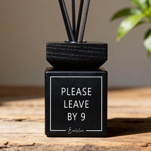 Könnte beinhalten: Eine weiße Keramik-Tasse mit schwarzem Henkel und dem Text "But First, Coffee" in schwarzer, handschriftlicher Schrift. Die Tasse steht auf einer weißen Oberfläche.