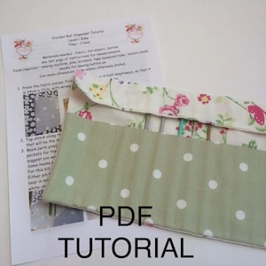 May include: A crochet roll organizer tutorial with a floral and polka dot fabric design. The tutorial is on a white sheet of paper with the words "PDF TUTORIAL" in large black letters.