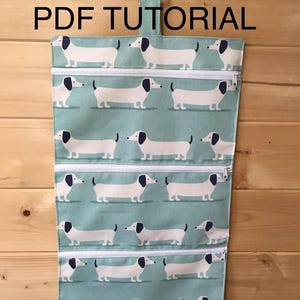 May include: A hanging organizer with four zippered compartments. The organizer is light blue with a repeating pattern of white dachshund dogs with black ears and tails. The text "PDF TUTORIAL" is printed at the top.
