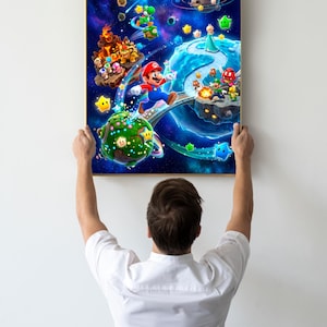 May include: A rectangular framed wall art print featuring a vibrant space scene with Mario, Luigi, Princess Rosalina, Bowser, and Yoshi navigating various planets and floating islands against a deep blue cosmic background filled with stars.