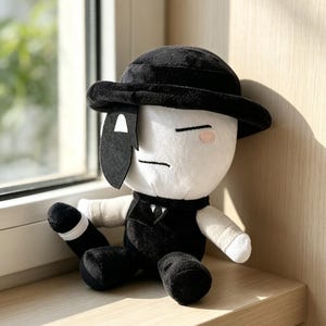 以下が含まれることがあります： 白い顔に片目を覆う黒いマスクをしたぬいぐるみ。黒い帽子をかぶり、白いシャツの上に黒いベストを着ている。シンプルな刺繍の目とピンクの頬のディテールがあり、黒い手足と白い袖口が特徴的である。