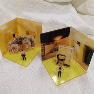 May include: Two acrylic diorama sets featuring yellow-toned interior scenes. One set depicts a cluttered room with a figure, while the other shows a dark room with a television screen displaying A24 and a figure standing on a bright yellow base.