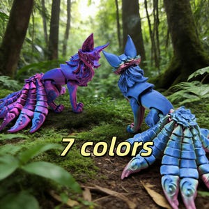 May include: Two fantasy fox figurines in a forest setting. One is purple and blue, the other blue. The text "7 colors" is displayed. The figurines have multiple tails and are posed on a bed of green moss.