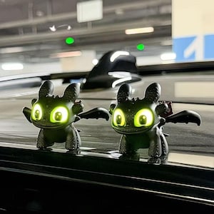 May include: Two black dragon figurines with glowing green eyes and wings. The figurines are posed in a playful stance, with intricate details on their bodies. The background is blurred, focusing attention on the dragon figures.