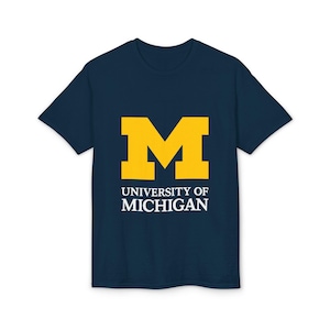 May include: Navy blue t-shirt featuring a large yellow "M" logo and the words "UNIVERSITY OF MICHIGAN" in white. The shirt is a classic crew neck style, suitable for casual wear. The design is centered on the front of the shirt.
