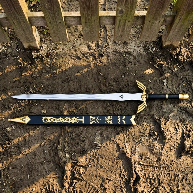 May include: A silver-toned metal sword with a black leather-wrapped handle, a gold-colored crossguard, and a pommel. Below the sword lies a black scabbard featuring gold-colored decorative engravings and a gold-colored metal tip and throat.