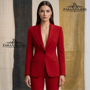 Op de afbeelding: Een felrood pak, bestaande uit een blazer met één knoop en een bijpassende broek. Het pak heeft een klassiek ontwerp met een gekerfde revers en zakken. De merknaam "ZARAATELIERS" is zichtbaar in de hoeken.