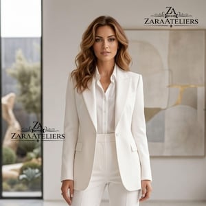 May include: A woman wearing a white suit, consisting of a blazer, a button-down shirt, and matching pants. The blazer has a classic design with a notched lapel and a single-button closure. The suit is from ZARAATELIERS.