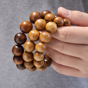 May include: A bracelet composed of multiple smooth, spherical wooden beads in varying shades of brown, ranging from light tan to deep dark chocolate. The beads are strung together in a circular formation, showcasing natural wood grain patterns.