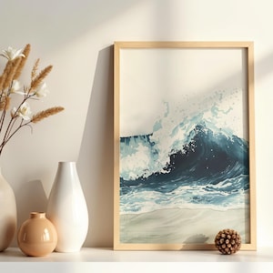 以下が含まれることがあります： 砂浜に打ち寄せる水彩画の波を描いた、額入りのアートプリント。アートワークは青と白の色合いを使用し、薄いベージュ色のフレームが付いています。プリントは白い棚に飾られており、装飾的な花瓶と松ぼっくりが並んでいます。