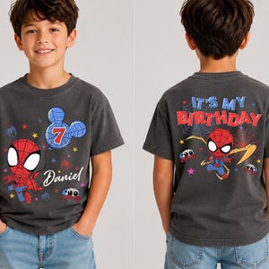 May include: A charcoal gray t-shirt featuring a cartoon Spider-Man graphic. The front displays a blue Mickey Mouse-shaped balloon with the number 7 and the name Daniel. The back features Spider-Man with the text IT'S MY BIRTHDAY and spiderwebs.