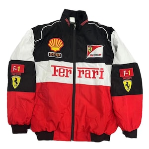 May include: A Ferrari racing jacket in red, white, and black. The jacket features the Ferrari logo, Shell and OMP patches, and F-1 patches. The jacket has a full zip and a stand-up collar.