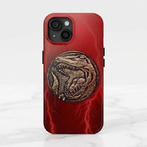 May include: Red iPhone case featuring a gold-colored coin with a detailed dinosaur design. The case has a red lightning bolt pattern and a camera cutout. The case is designed for a smartphone.