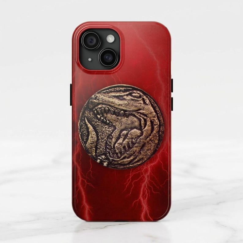 May include: Red iPhone case featuring a gold-colored coin with a detailed dinosaur design. The case has a red lightning bolt pattern and a camera cutout. The case is designed for a smartphone.