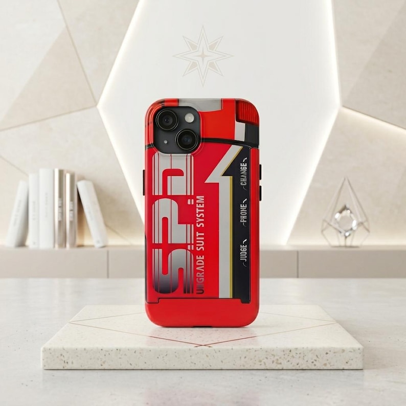 Puede incluir: Una funda roja para tel&eacute;fono con el texto "SPF1 UPGRADE SUIT SYSTEM" en blanco y gris. La funda tiene detalles en negro y las palabras "JUDGE", "PROBE" y "CHANGE" impresas en el lateral. La funda est&aacute; sobre una superficie blanca.
