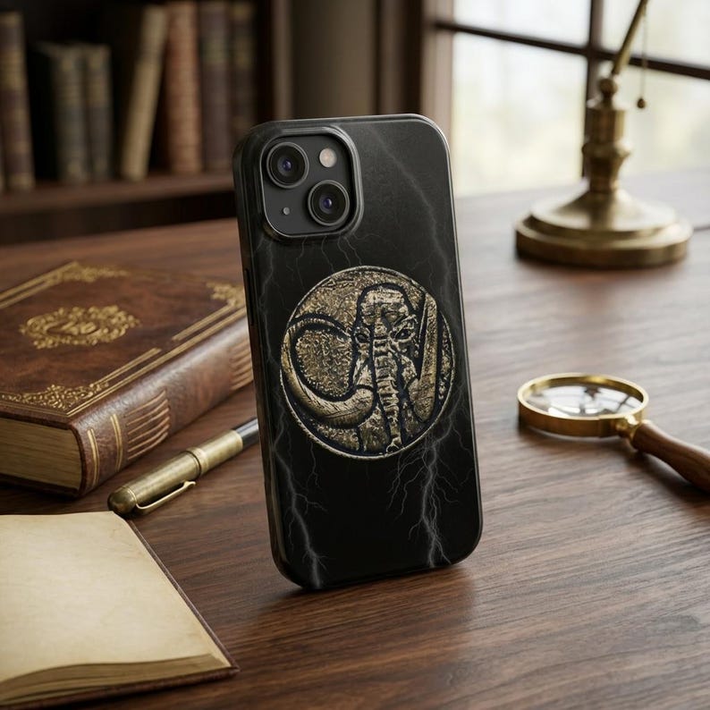 May include: Black iPhone case with a gold-colored mammoth design. The case has a marble-like texture with lightning bolt accents. The mammoth is in a circular emblem. The case is on a wooden surface.