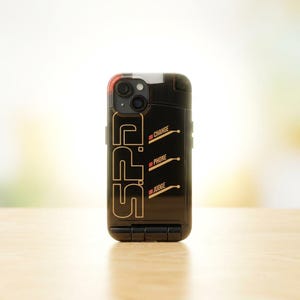Puede incluir: Funda de tel&eacute;fono negra con letras y detalles dorados. La funda presenta las letras "S.P.D." verticalmente, con las palabras "CHANGE", "PHONE" y "JUDGE" debajo. La funda tiene un dise&ntilde;o rectangular con un recorte para la c&aacute;mara.