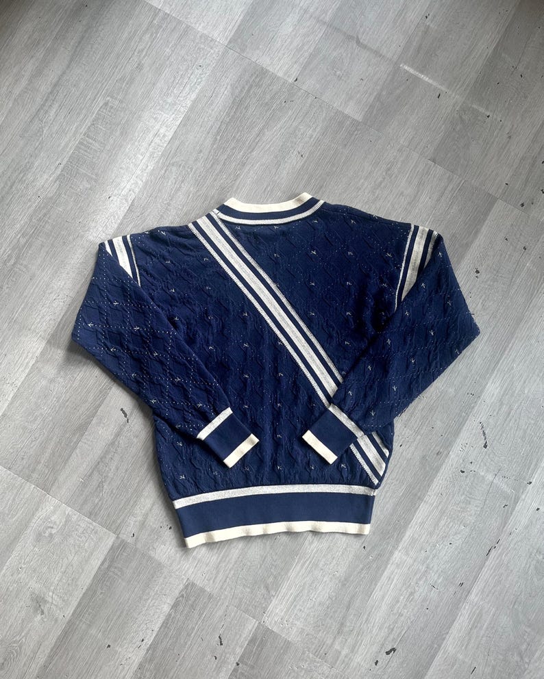 May include: Navy blue sweater with white stripes and trim. The sweater features a textured knit pattern and a crew neck. The sleeves and hem have white and navy blue bands. A diagonal white stripe runs across the front.