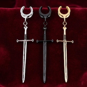 May include: Three sword-shaped earrings in silver, black, and gold. Each earring has a curved top, a chain, and a detailed sword pendant. The earrings are set against a dark red background.