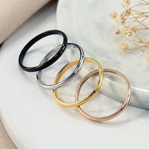 以下が含まれることがあります： 黒い持ち手と「But First, Coffee」のテキストが黒い太字で書かれた白いセラミックマグ。マグは木製の表面に置かれています。マグの高さは約10cmです。