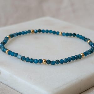 Peut inclure: Un bracelet délicat composé de petites perles bleues facettées, entrecoupées de perles dorées. Le bracelet est présenté sur une surface blanche, mettant en valeur son design simple mais élégant. Les perles mesurent environ 0,5 cm de diamètre.