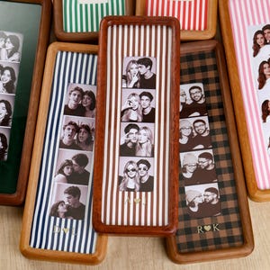 Puede incluir: Una colección de marcos de fotos rectangulares de madera, cada uno con una tira vertical de cuatro fotografías en blanco y negro. Los marcos presentan varios fondos estampados, incluyendo rayas y cuadros, con iniciales doradas y un corazón.