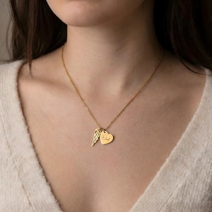 May include: Gold-colored necklace with a delicate chain. The pendant features a heart charm with the word "Dad" engraved, and a wing charm. The necklace is worn around the neck.
