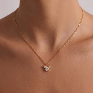 K&ouml;nnte beinhalten: Eine goldfarbene Halskette mit einem Anh&auml;nger in Form eines M&auml;usekopfes. Der Anh&auml;nger hat einen gro&szlig;en, runden, klaren Edelstein in der Mitte, flankiert von zwei kleineren Edelsteinen. Die Kette ist filigran und gedreht.