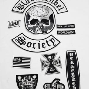 Könnte beinhalten: Eine Sammlung von schwarz-weißen, gestickten Aufnähern mit verschiedenen Designs und Texten. Die Aufnäher zeigen einen Totenkopf, die Worte "Black Label Society", "Society", "Doom Crew Inc" und "Berserker".