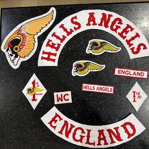Puede incluir: Un conjunto de parches de Hells Angels, con el icónico logotipo de la calavera alada. Los parches incluyen las palabras "Hells Angels" y "England" en letras rojas sobre fondos blancos. Otros parches muestran "1%" y "HAMC".