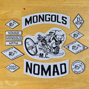 Può includere: Una collezione di toppe ricamate bianche e nere, tra cui una toppa grande con la scritta "MONGOLS" e una toppa centrale raffigurante un motociclista su una moto. Altre toppe includono "NOMAD" e "M.C."