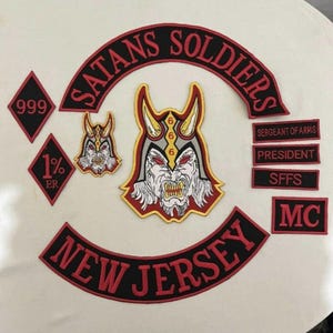 May include: A collection of embroidered patches with a biker theme. The patches feature the words "SATANS SOLDIERS" and "NEW JERSEY" in red lettering on a black background. Other patches include a devil face and the numbers "999" and "1% ER".