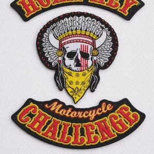 Puede incluir: Parches bordados con una calavera que lleva un tocado nativo americano y una bandana amarilla. Los parches incluyen el texto "HOKA HEY" y "Motorcycle Challenge" en rojo y amarillo.